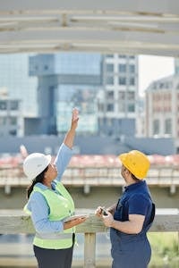 Two architects discussing plans at a city construction site with high-rise buildings.